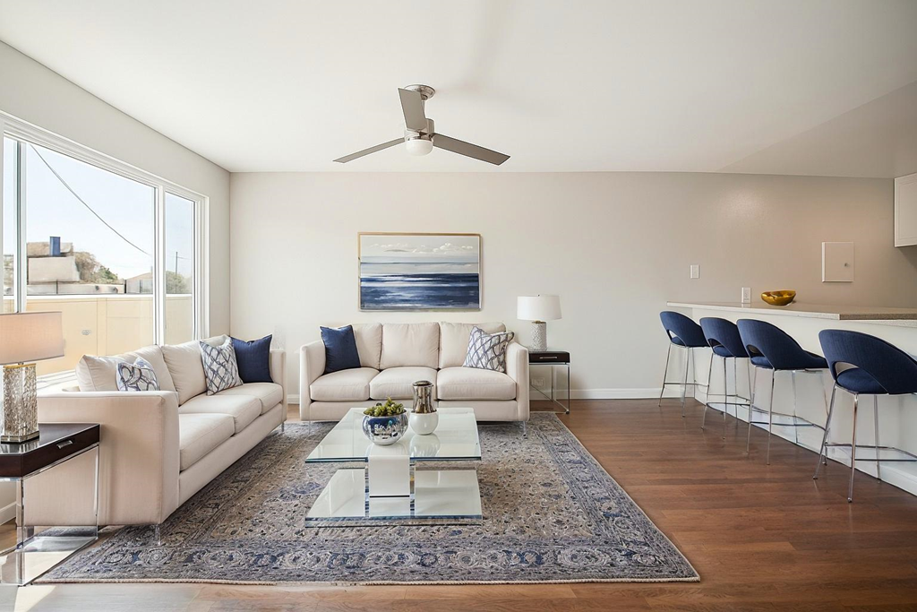 A modern living room with a white sofa set, a glass coffee table, and a ceiling fan.