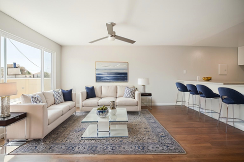 A modern living room with a white sofa set, a glass coffee table, and a ceiling fan.