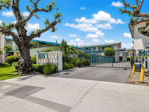 A tree stands in front of a white building with a blue roof.