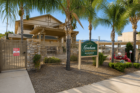 A sign for Graham Apartments is in front of a building with a fence and palm trees.