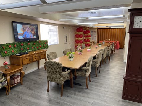 A conference room with a long table and chairs, a television on the left, and a clock on the right.
