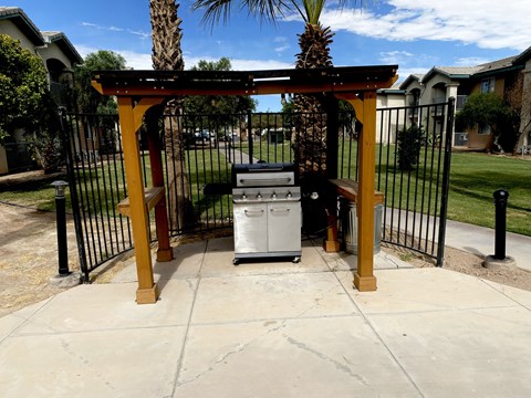 A white trash can sits under a wooden pergola.