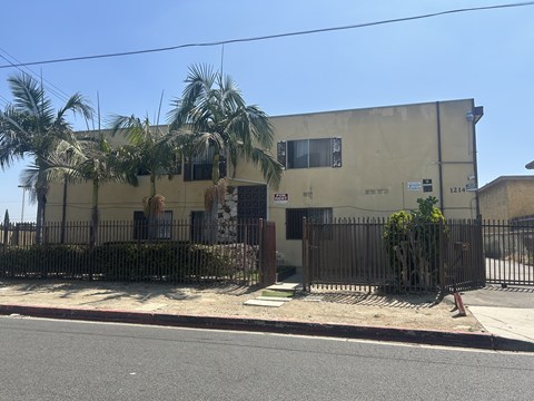 A building with a fence and palm trees in front.