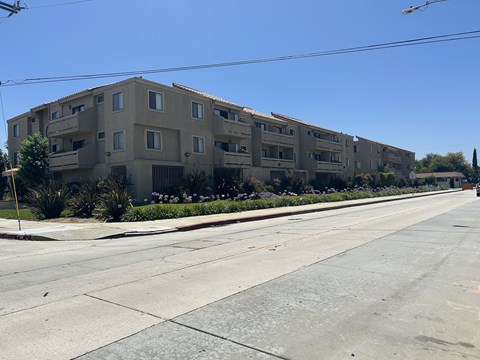 A long building with balconies is on the side of a street.