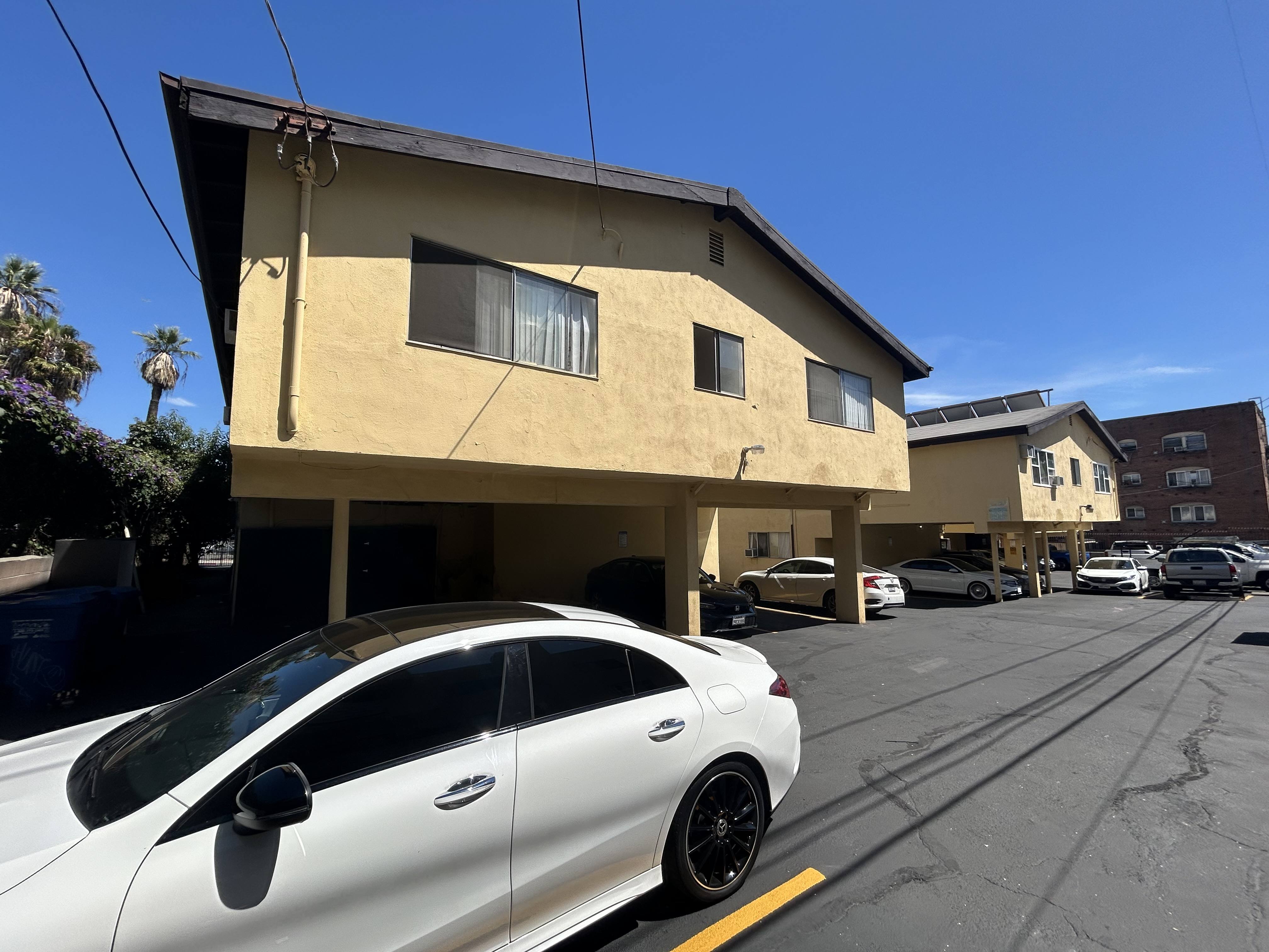 A white car is parked in a parking lot in front of a yellow building.