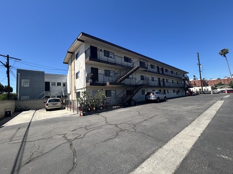 A parking lot with a white building and a car parked in front.