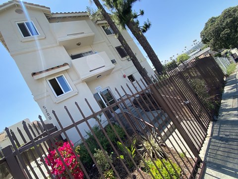 A tall white building with a brown gate and plants in front.