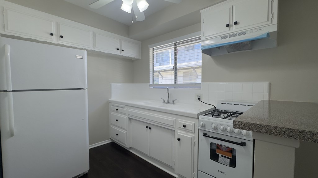 A white kitchen with a fridge, stove, and sink.