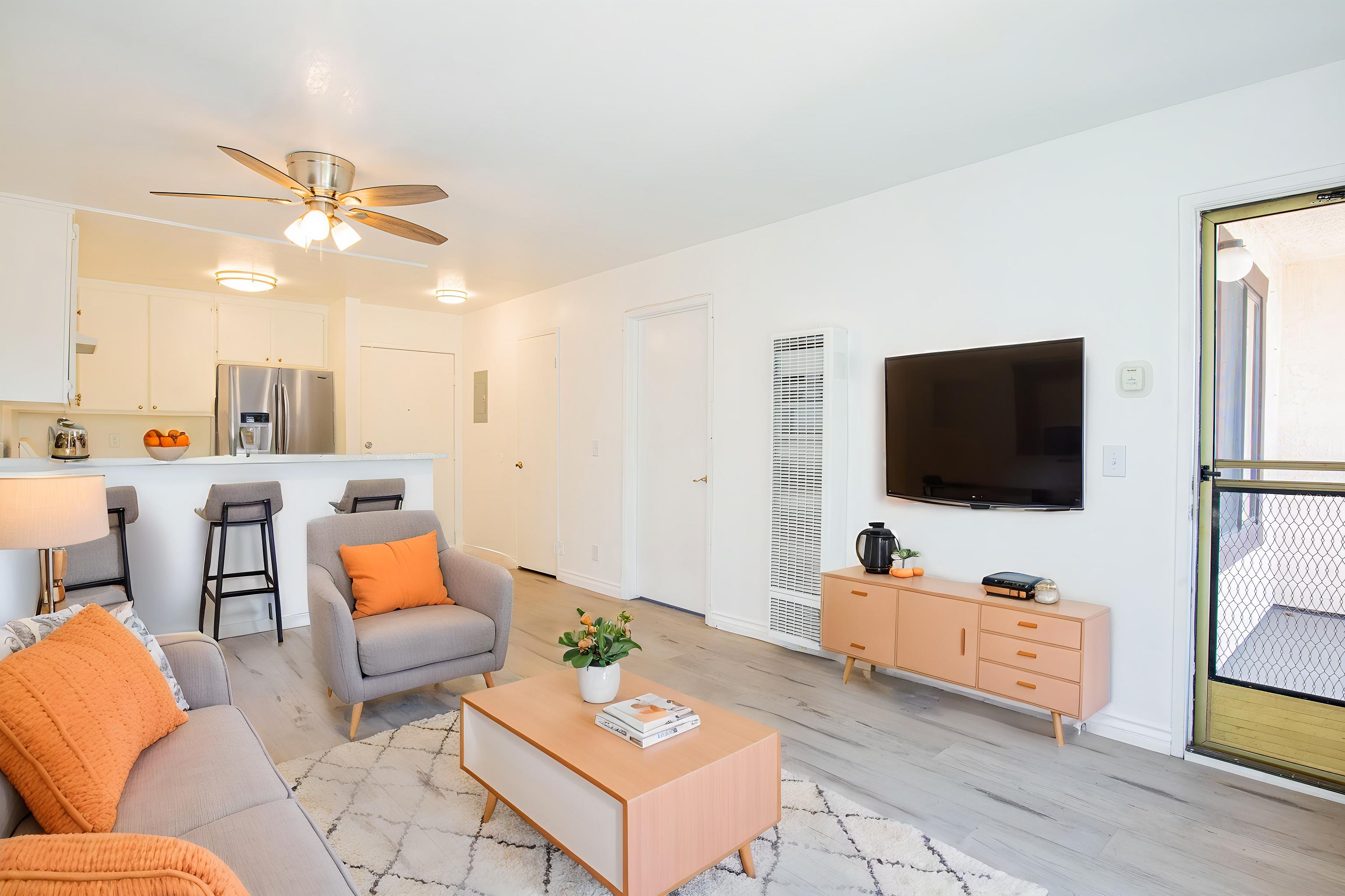 A living room with a grey couch, orange pillows, a pink coffee table, and a television.