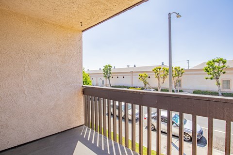 A balcony with a metal railing and a view of a street with cars and buildings.
