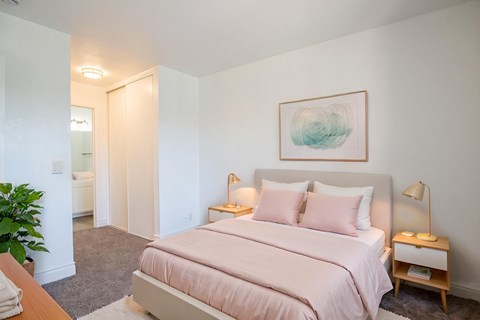 A bedroom with a pink bed and a painting on the wall.