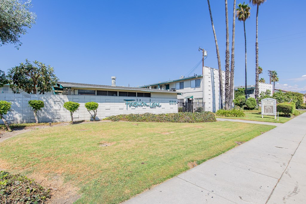A building with a wall covered in graffiti is surrounded by a green lawn and palm trees.