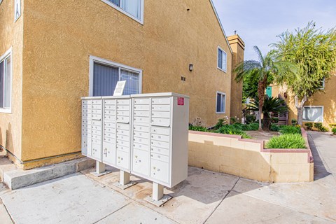 A mailbox is on the sidewalk in front of a tan building.