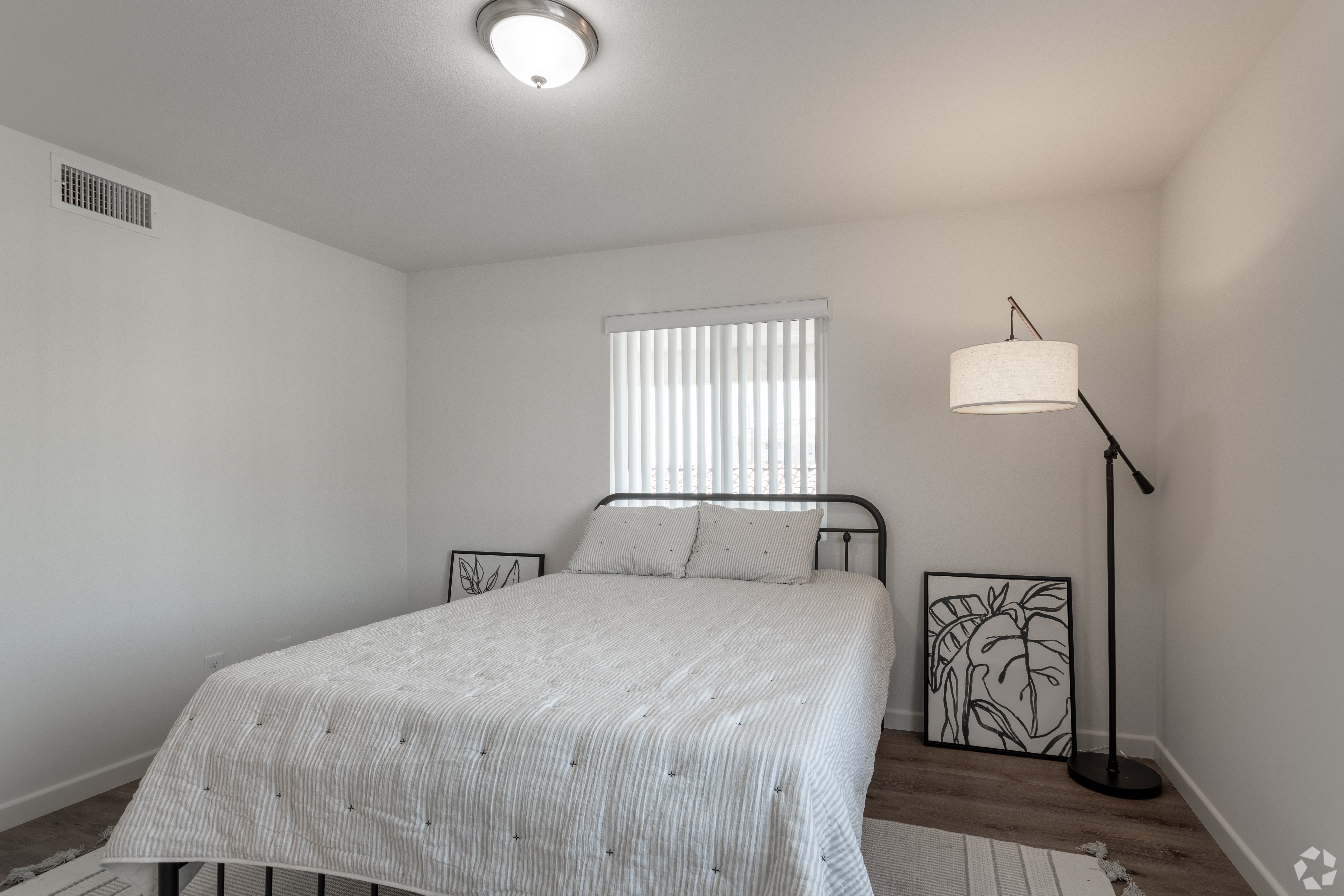 A bedroom with a bed, a lamp, and a window with blinds.