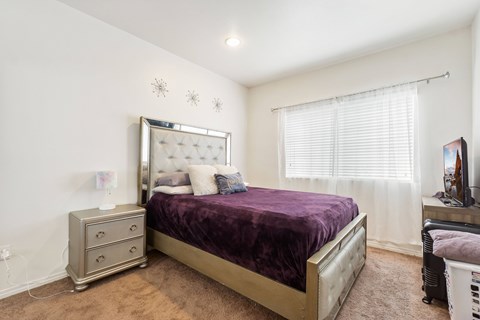 A bedroom with a purple bedspread and a white bed frame.