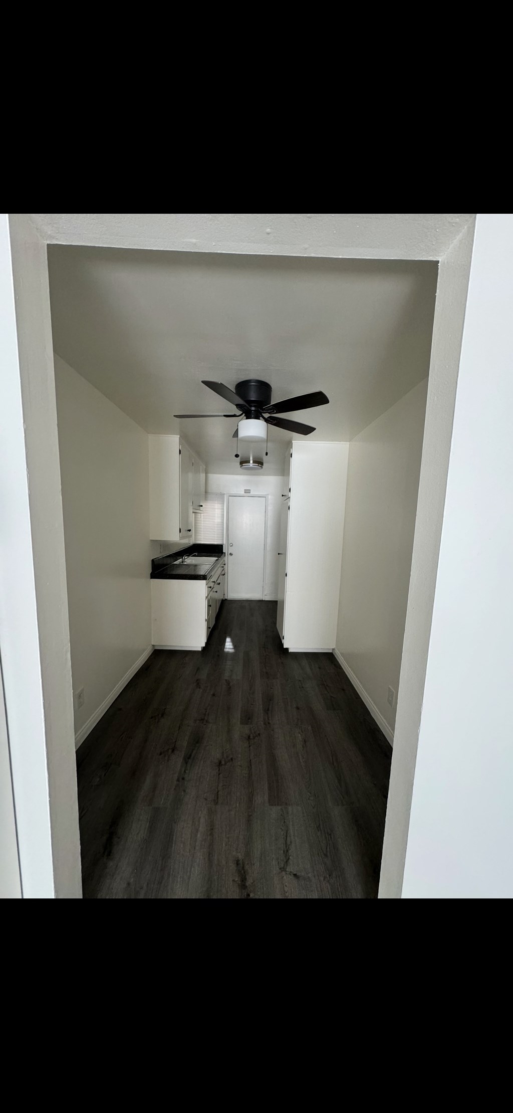 A long hallway with a ceiling fan and a white door at the end.