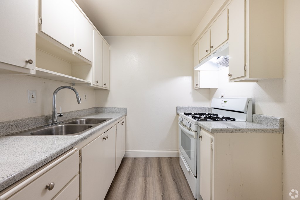 A small kitchen with a sink, stove, and cabinets.