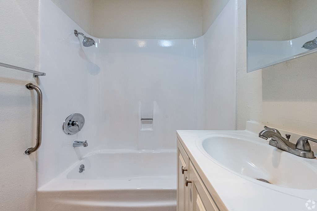 A white bathroom with a tub, sink and mirror.