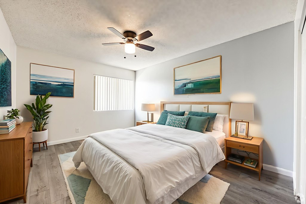 A bedroom with a large bed, a ceiling fan, and two pictures on the wall.