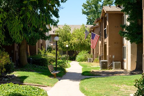 a pathway lined with green grass and trees in front of an apartment building at Oak Terrace Senior Apts, Hemet