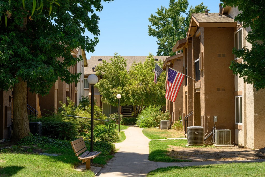 a pathway with a bench and trash cans in front of an apartment building at Oak Terrace Senior Apts, California, 92543