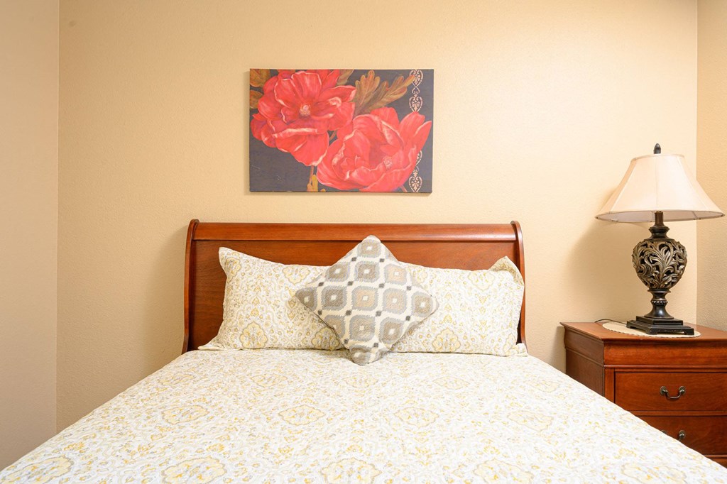 a bedroom with a bed and a nightstand with a lamp at Oak Terrace Senior Apts, Hemet, CA 92543