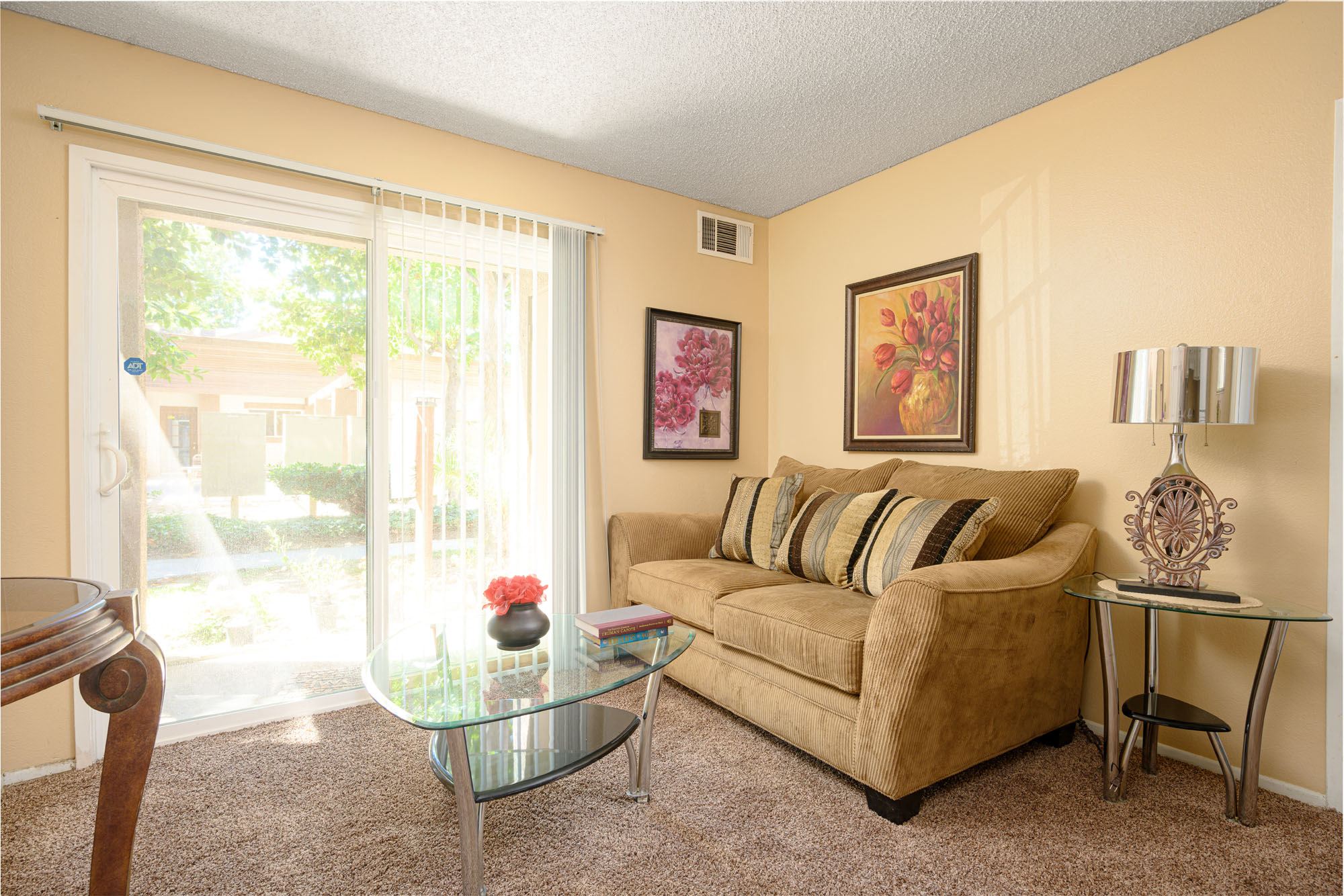 A living room with a tan couch, glass coffee table, and a painting on the wall.