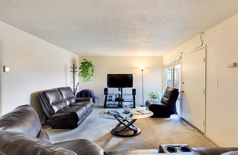 A living room with a black leather couch, a black chair, a black coffee table, and a flat screen TV.