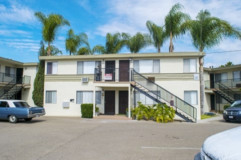 A blue car is parked in front of a building with a white facade and a balcony.