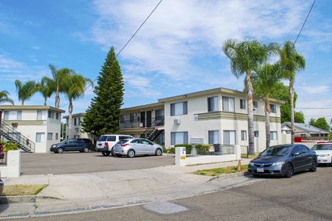 A residential street with cars parked on the side and apartment buildings in the background.