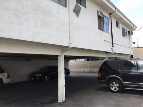A black car is parked in a garage under a white building.
