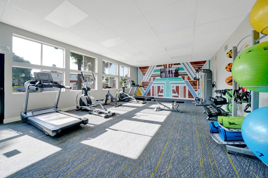 a gym with treadmills and weights in a room with windows at Sunnymead Apts Apartments, Moreno Valley