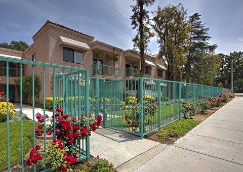 A green fence surrounds a building with red flowers in front.
