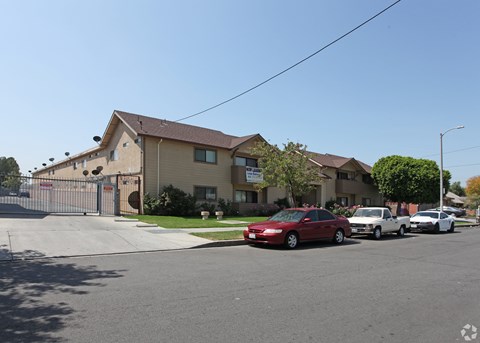A red car is parked in front of a house with a fence.