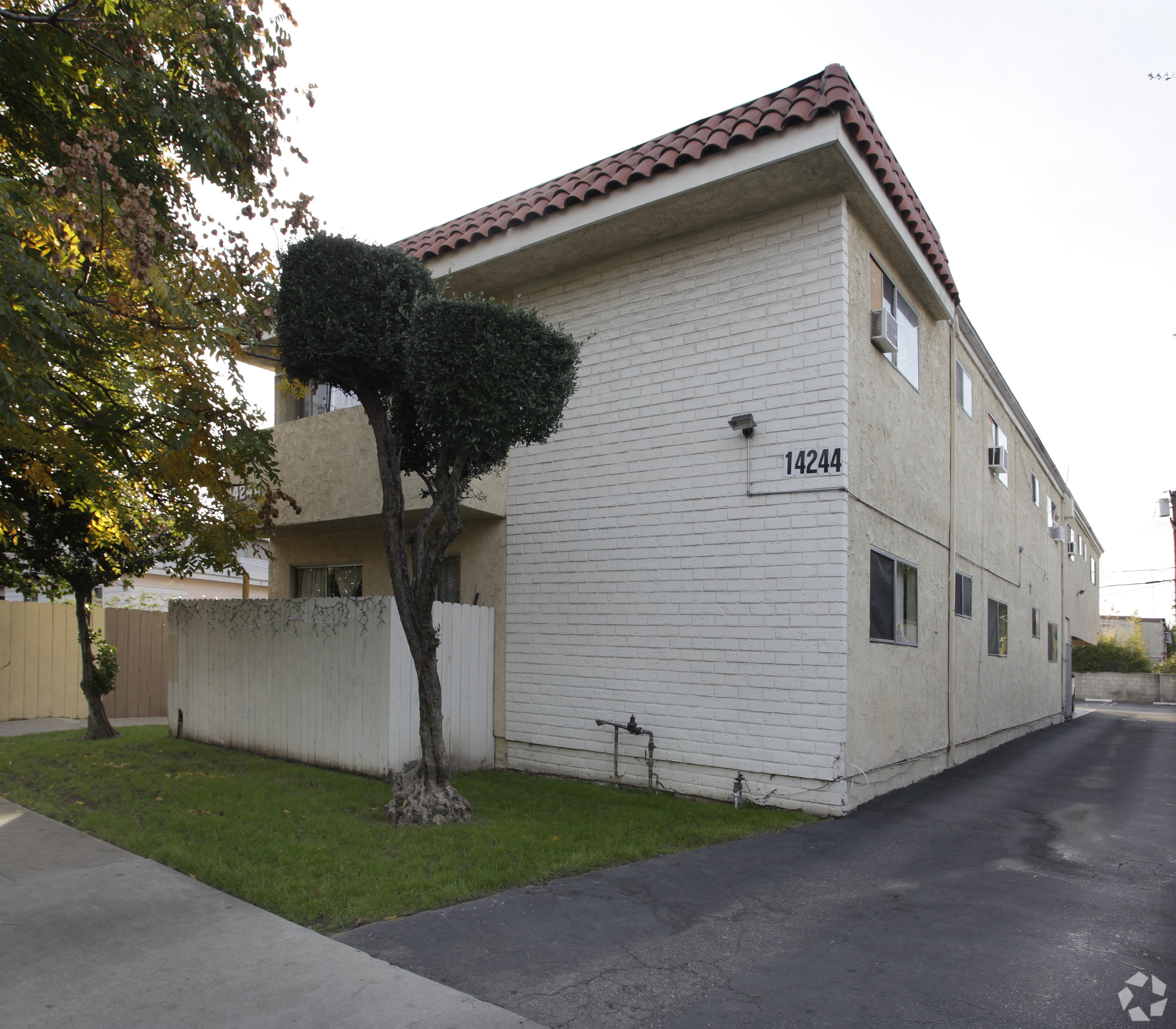 A white building with a red tile roof and a tree in front of it.