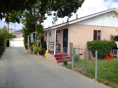 A residential street with a house on the right and a fence in front.