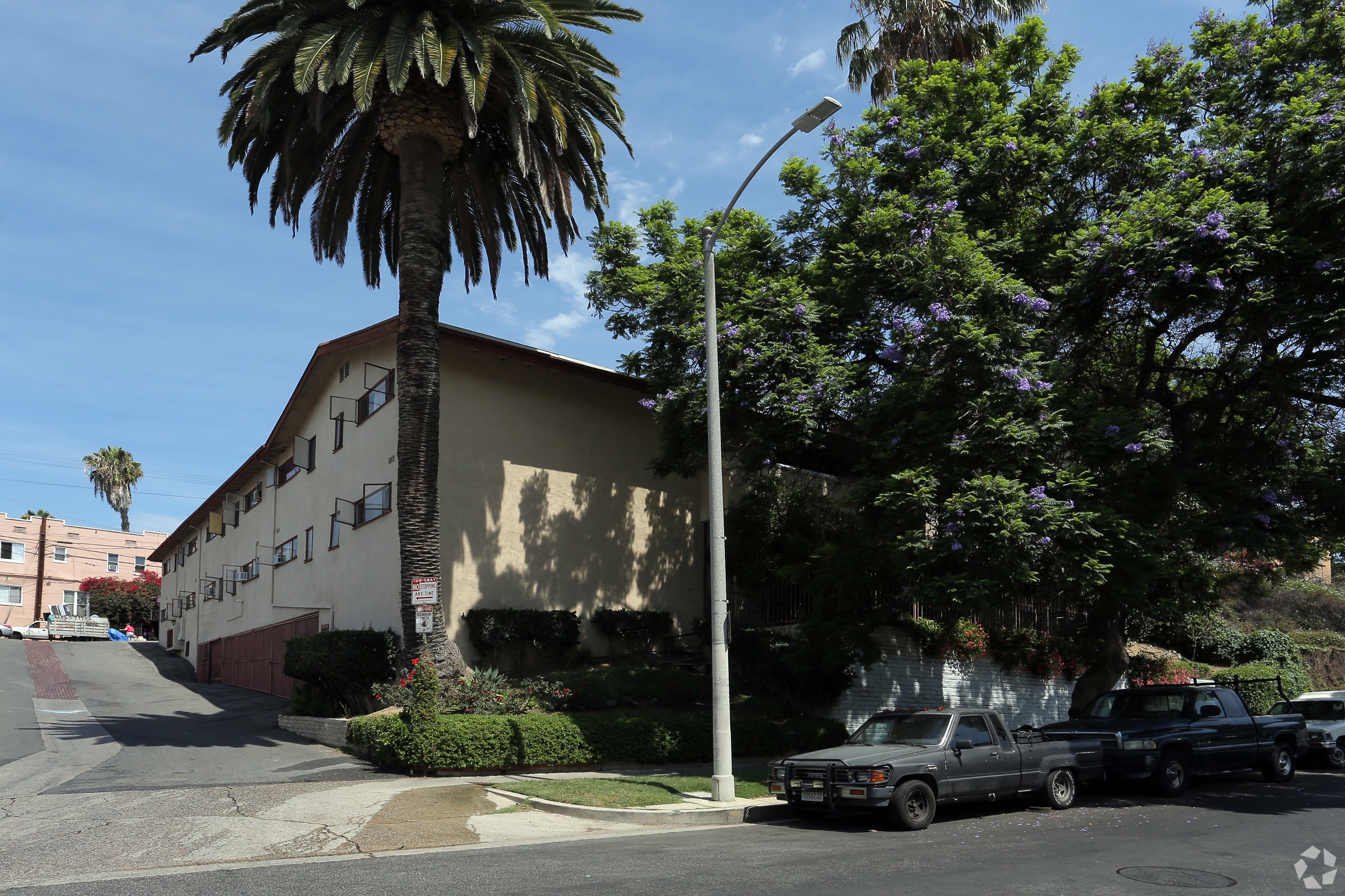 A palm tree stands in front of a tan building with a black truck parked in front of it.