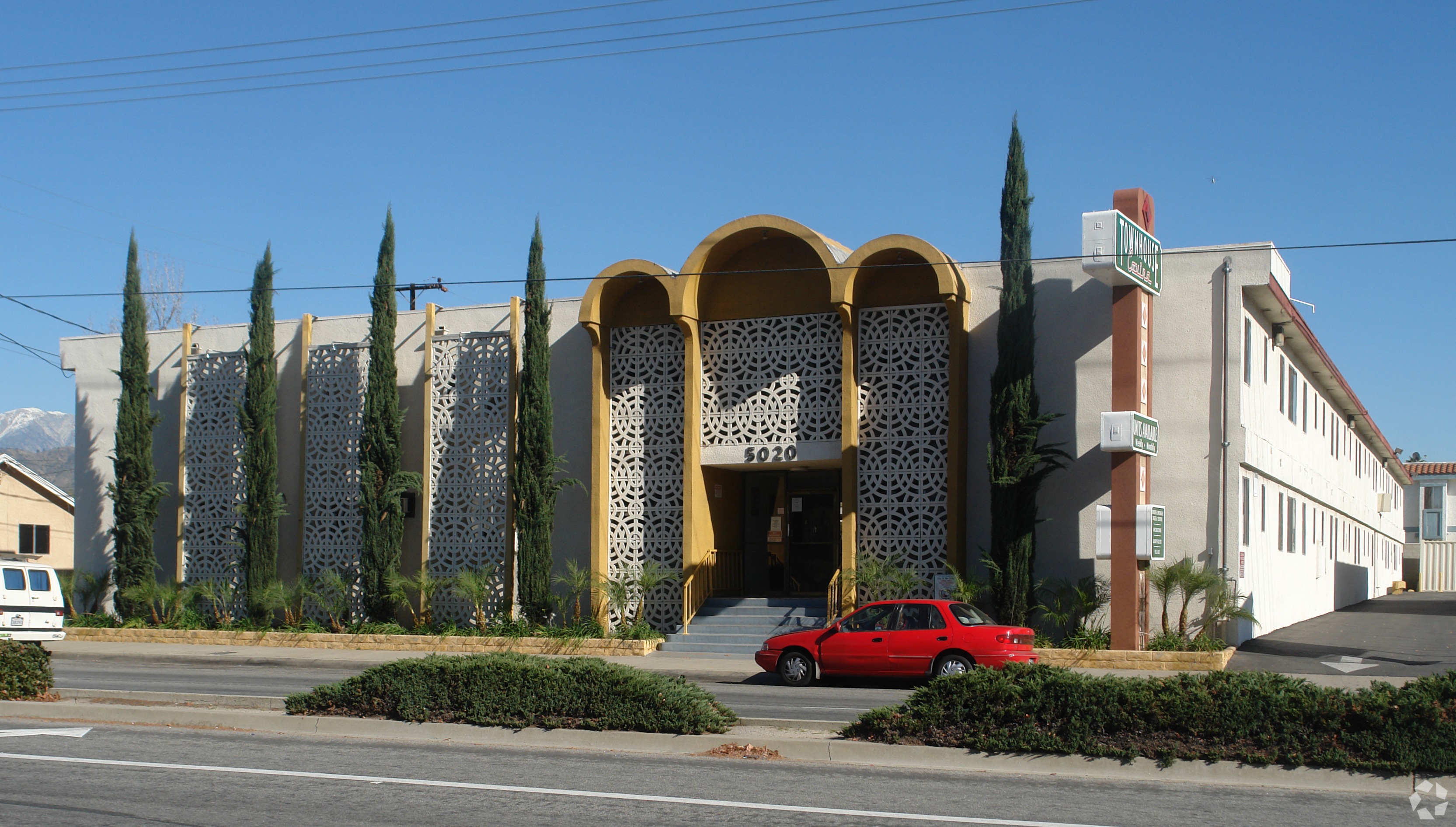 A red car is parked in front of a building with a yellow and white facade.