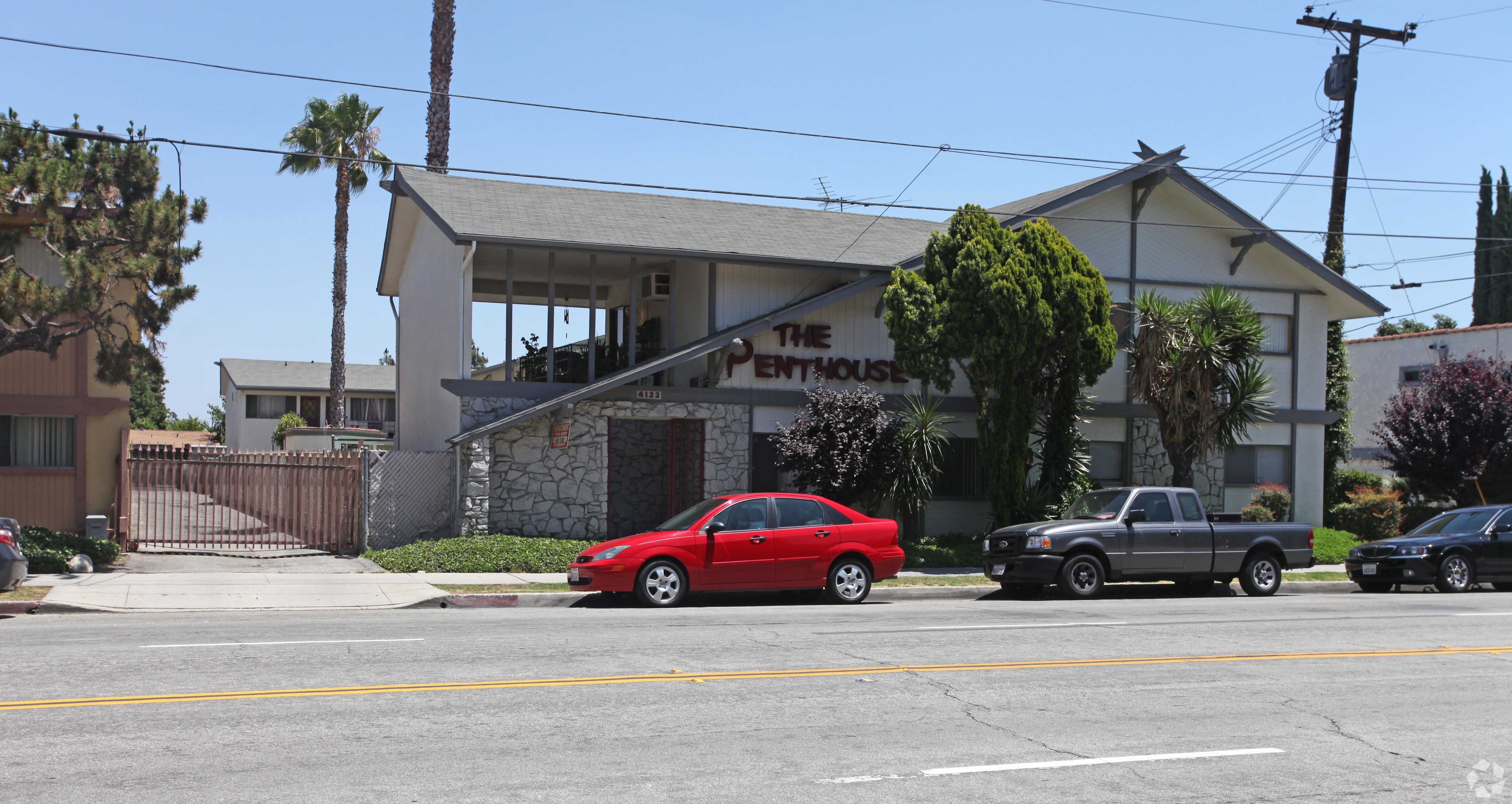A red car is parked in front of a white building with a sign that says "The Mentor House.".