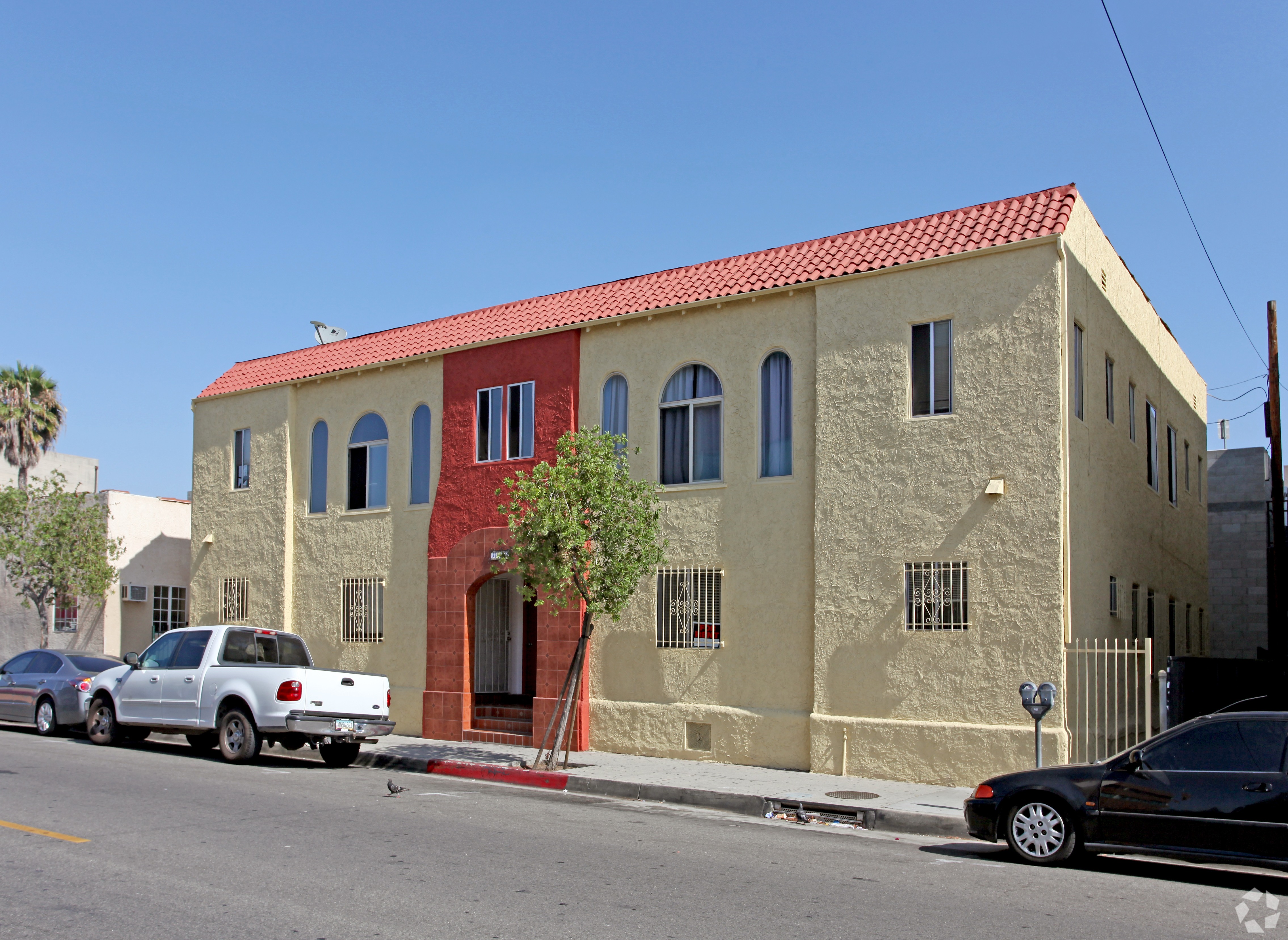 A white car is parked in front of a tan building with a red tile roof.