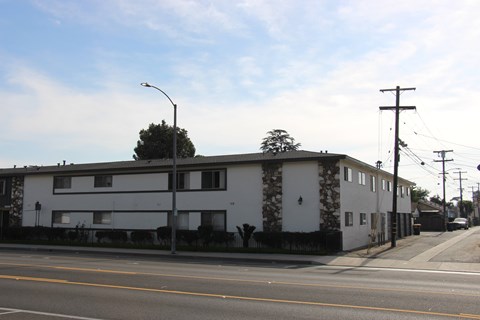 A street view of a residential area with a white building and a tree.