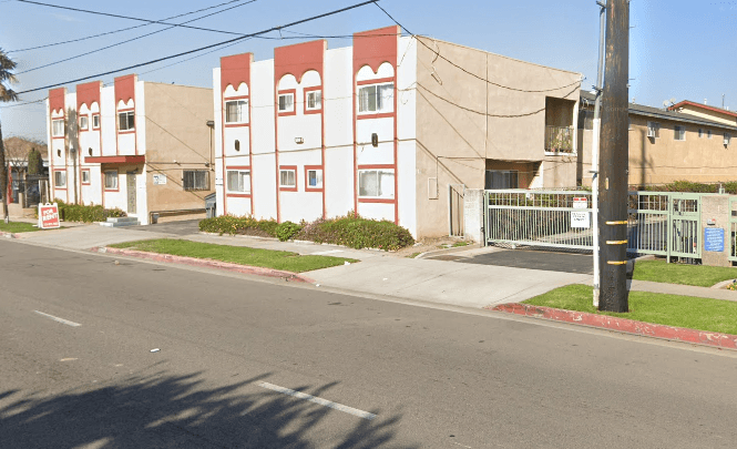 A street view of a red and white building with a green fence in front.