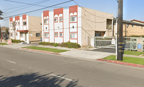 A street view of a red and white building with a green fence in front.