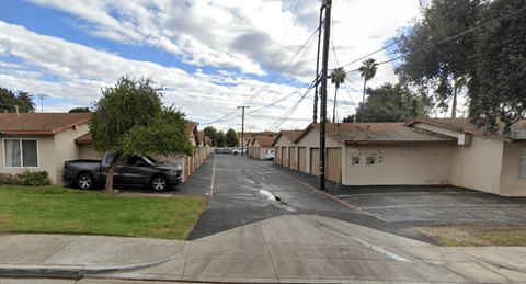 A residential street with houses on both sides and cars parked on the side.