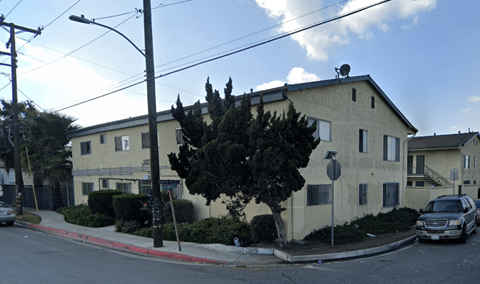 A street view of a residential area with a house, cars, and trees.