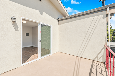 A balcony with a red railing and a sliding glass door leading to an empty room.