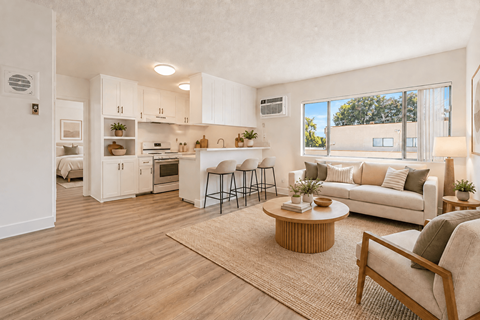 A well-lit, spacious kitchen and living room with wooden flooring and furniture.