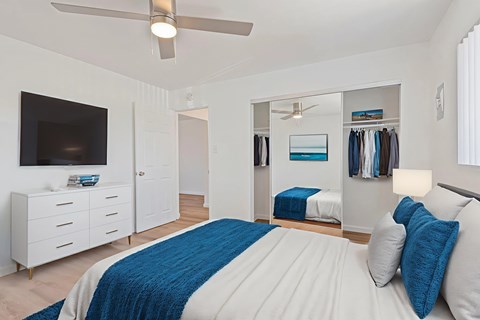 A bedroom with a bed, a dresser, a mirror, and a ceiling fan.
