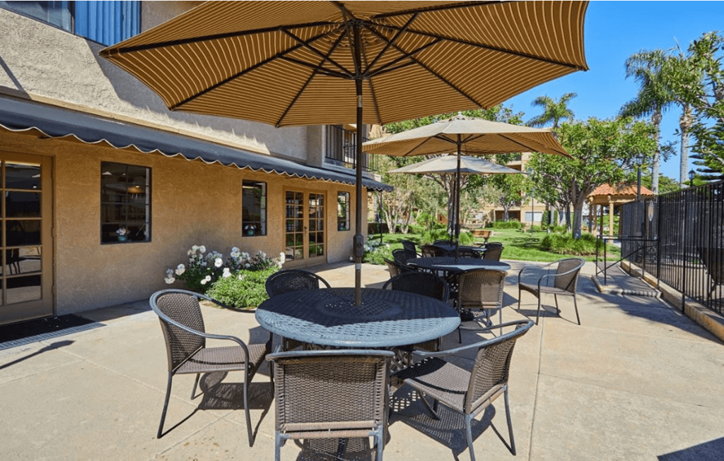 a patio with tables and umbrellas in front of a building at Huntington Terrace North Senior, Huntington Beach, CA
