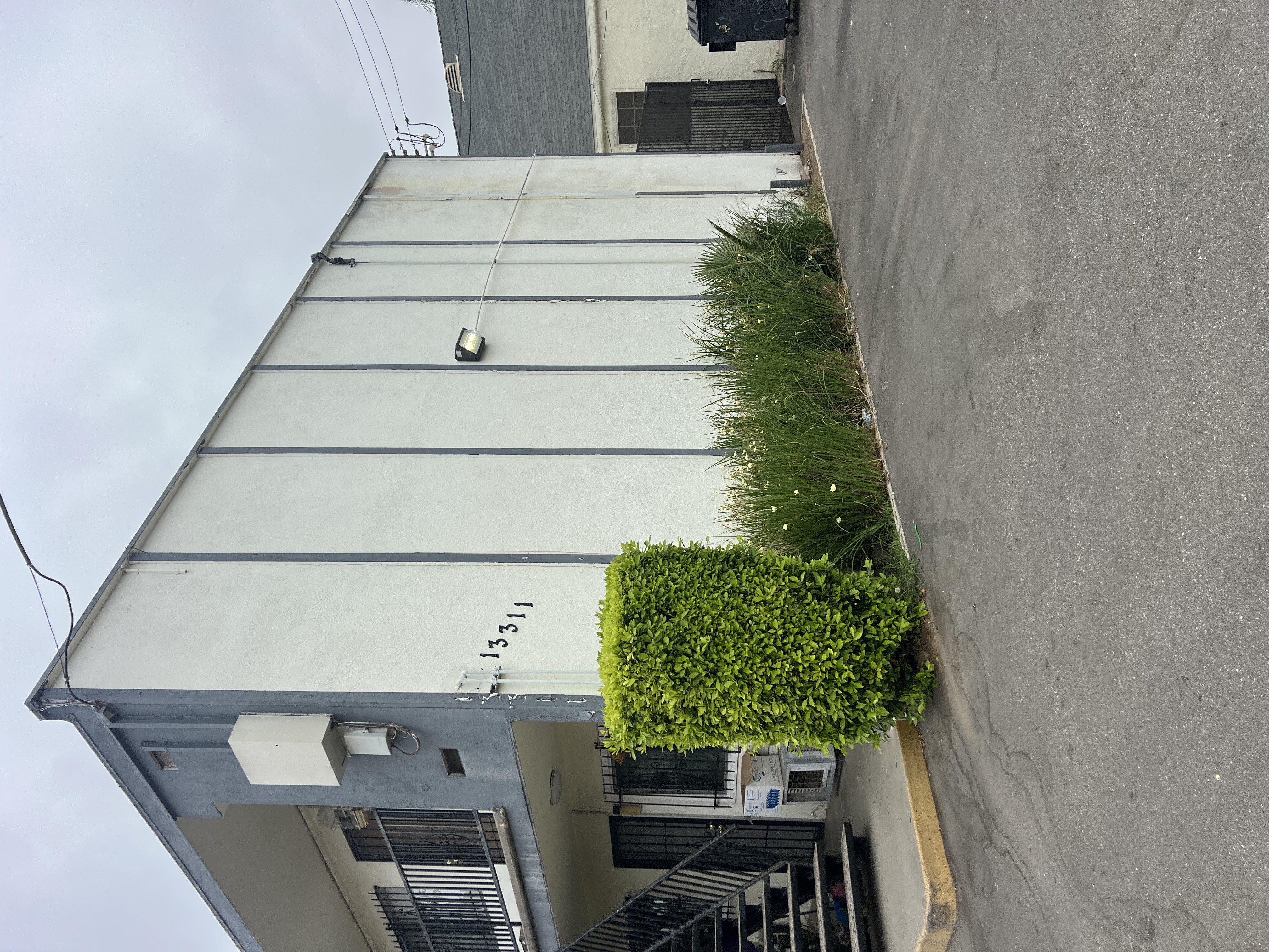 A grey building with a green bush on the side.